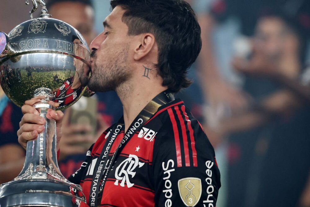Uruguaio concorre com Messi e Martínez 1 Arrascaeta em campo com a camisa do Flamengo, sorrindo e celebrando, representando sua performance no ano em que foi finalista do Prêmio Rei da América.